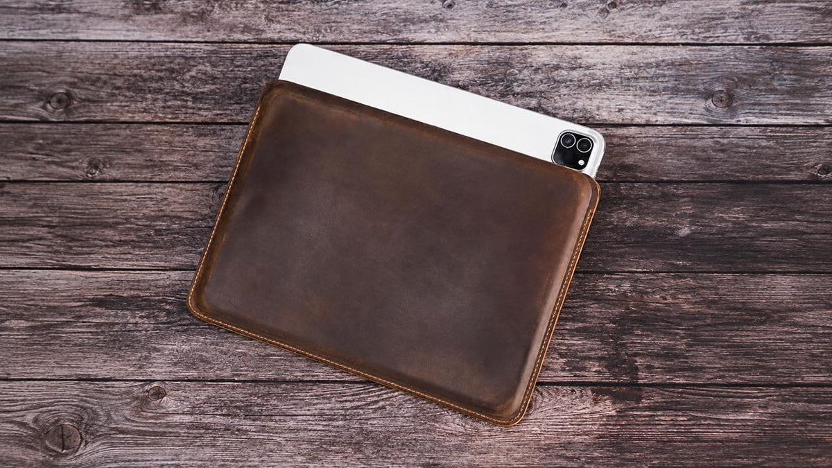 Brown leather iPad sleeve with a tablet partly inserted on a wooden tabletop